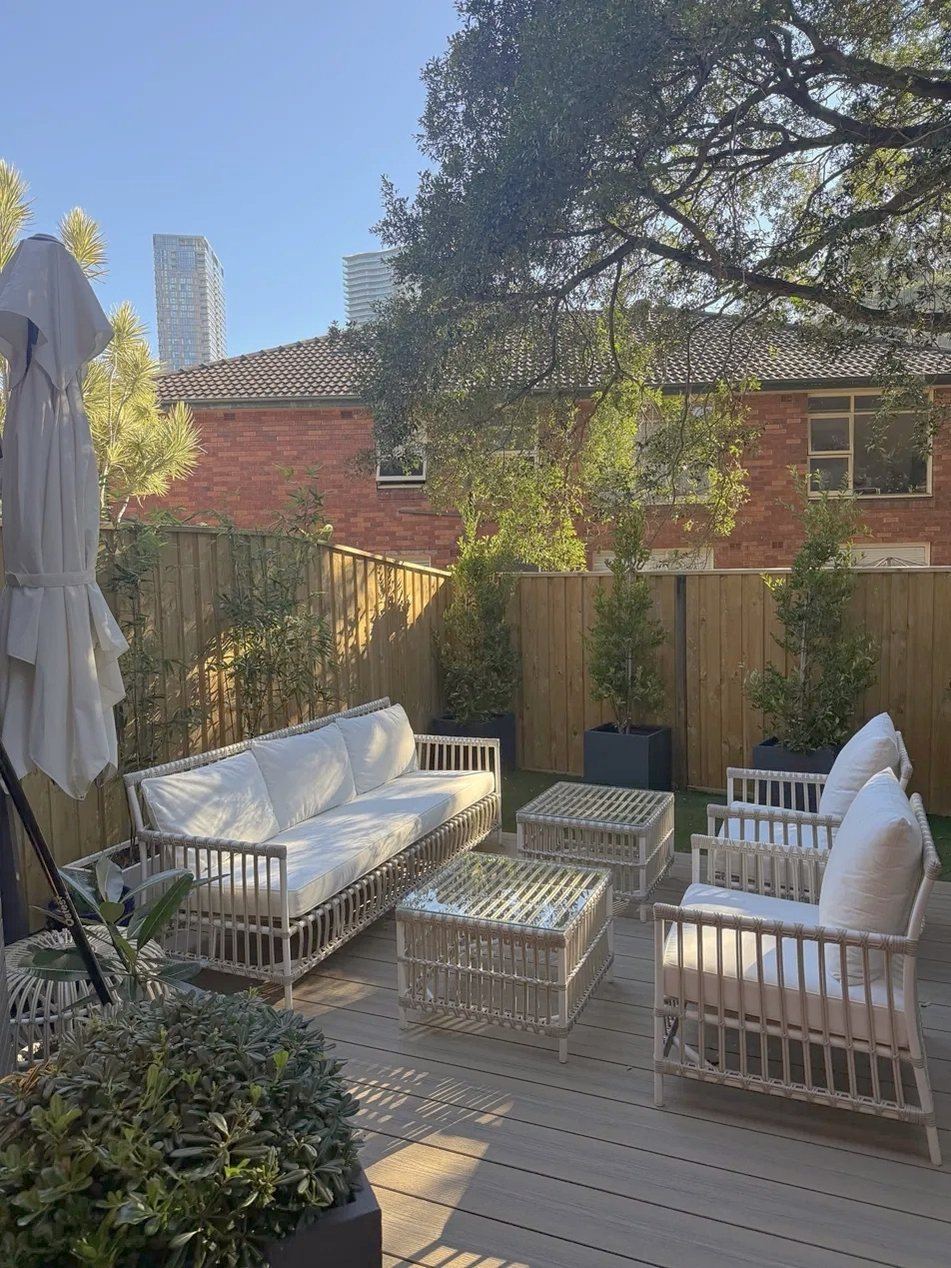 After: the rear courtyard, now a sunlit deck with new fencing, potted trees and outdoor lounge seating