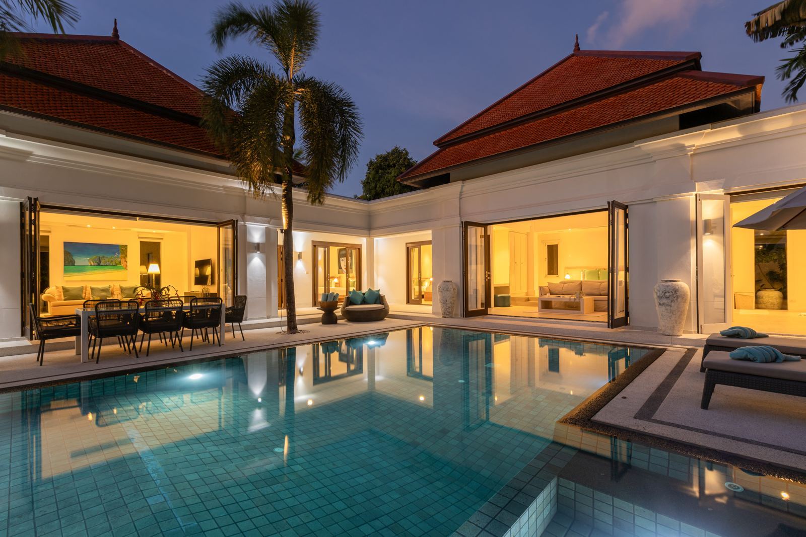 The renovated Phuket villa at dusk, with living areas opening onto the pool